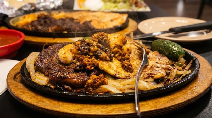 Sizzling fajitas with steak, chicken, shrimp, and chorizo on a hot plate with onions and a jalapeño.