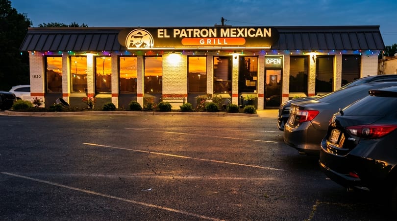 El Patron Mexican Grill exterior at dusk, with illuminated windows, colorful lights, and cars in the parking lot.