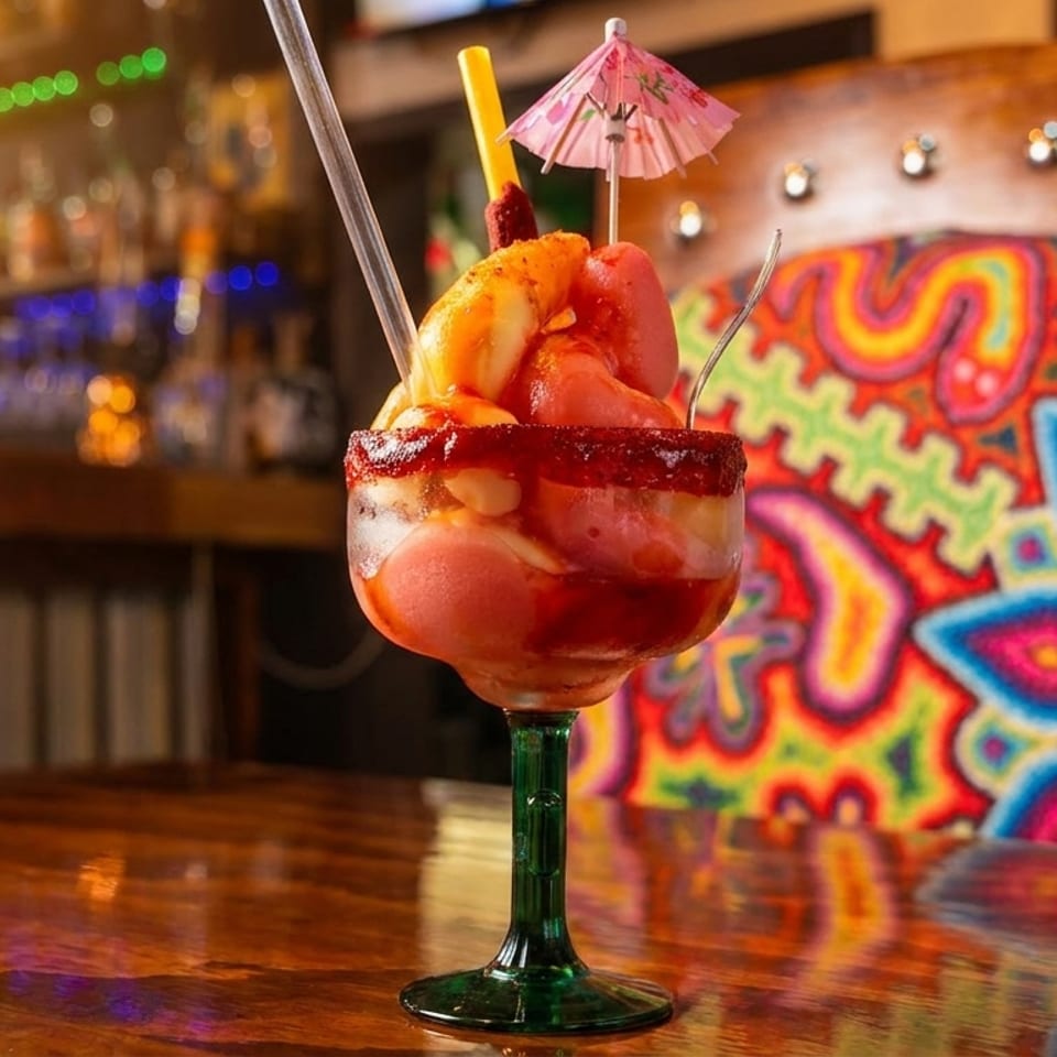 A colorful Mexican mangonada drink with a mini umbrella on a wooden table in a vibrant restaurant.